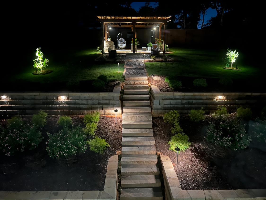 Evening view of illuminated terraced backyard with pergola seating